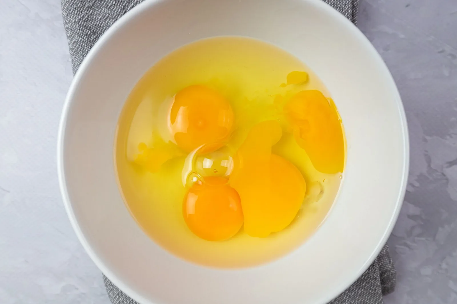 Raw egg yolks in a white ceramic bowl, ready to be beaten before freezing.